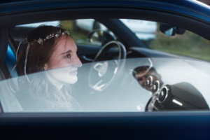 Die Braut sitzt im Hochzeitsauto und schaut zum Ehemann außerhalb des Autos, welcher sich in der halb heruntergelassenen Scheibe spiegelt.