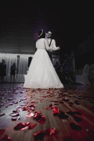 Im Hintergrund sieht man den Hochzeitstanz des Brautpaares, während im Vordergrund rotes Konfetti auf dem Holzboden liegt.