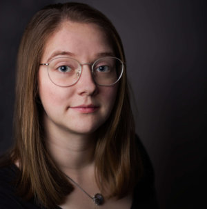 Business Portrait einer jungen Frau mit Brille vor dunklem Hintergrund.