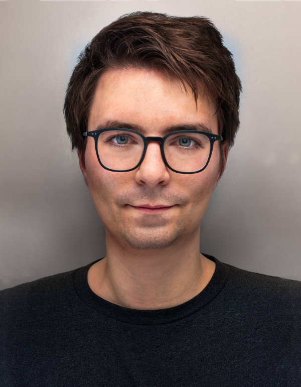 Portrait eines Mannes mit Brille und schwarzen Oberteil vor einem weißen Hintergrund.
