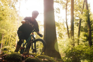 Erwartungsvoll steht ein Mountainbiker vor einer Abfahrt im Wald in Miltenberg und wird dramatisch von der Sonne im Rücken beleuchtet.