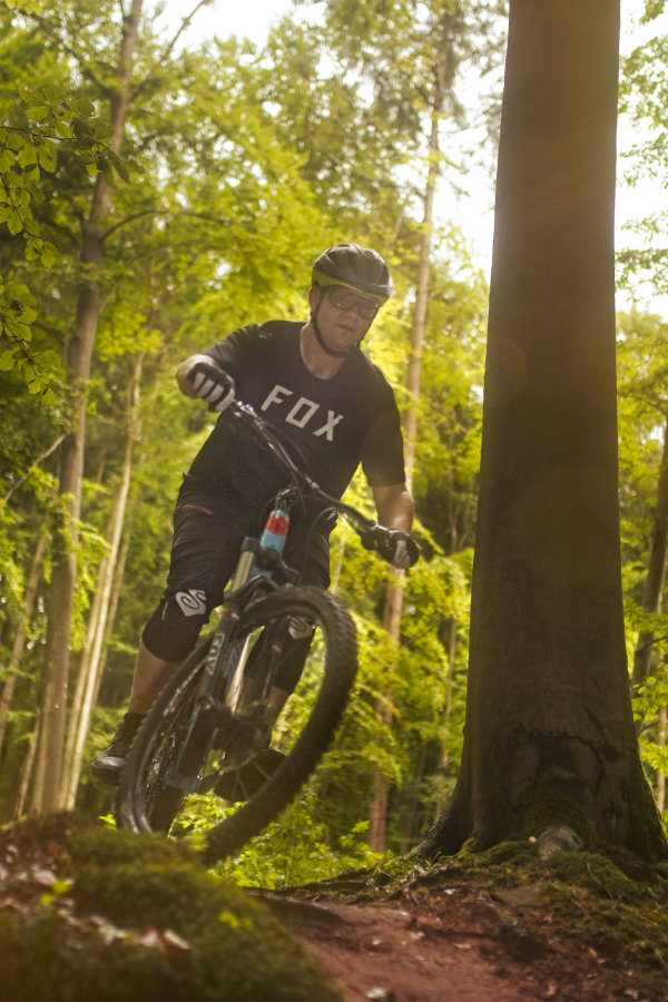 Mountainbike Fahrer macht einen kleinen Sprung im Sonnenlicht des Waldes in Miltenberg.