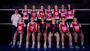 Klassisches Teamfoto in zwei Reihen eines Volleyball Team. Vordere Reihe sitzt auf einer Bank. Im Hintergrund ist ein Volleyballnetz zu sehen.