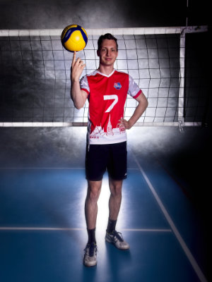 Mann posiert mit drehendem Volleyball auf dem rechten Zeigefinger vor einem Volleyballnetz. Im Hintergrund befindet sich Nebel.